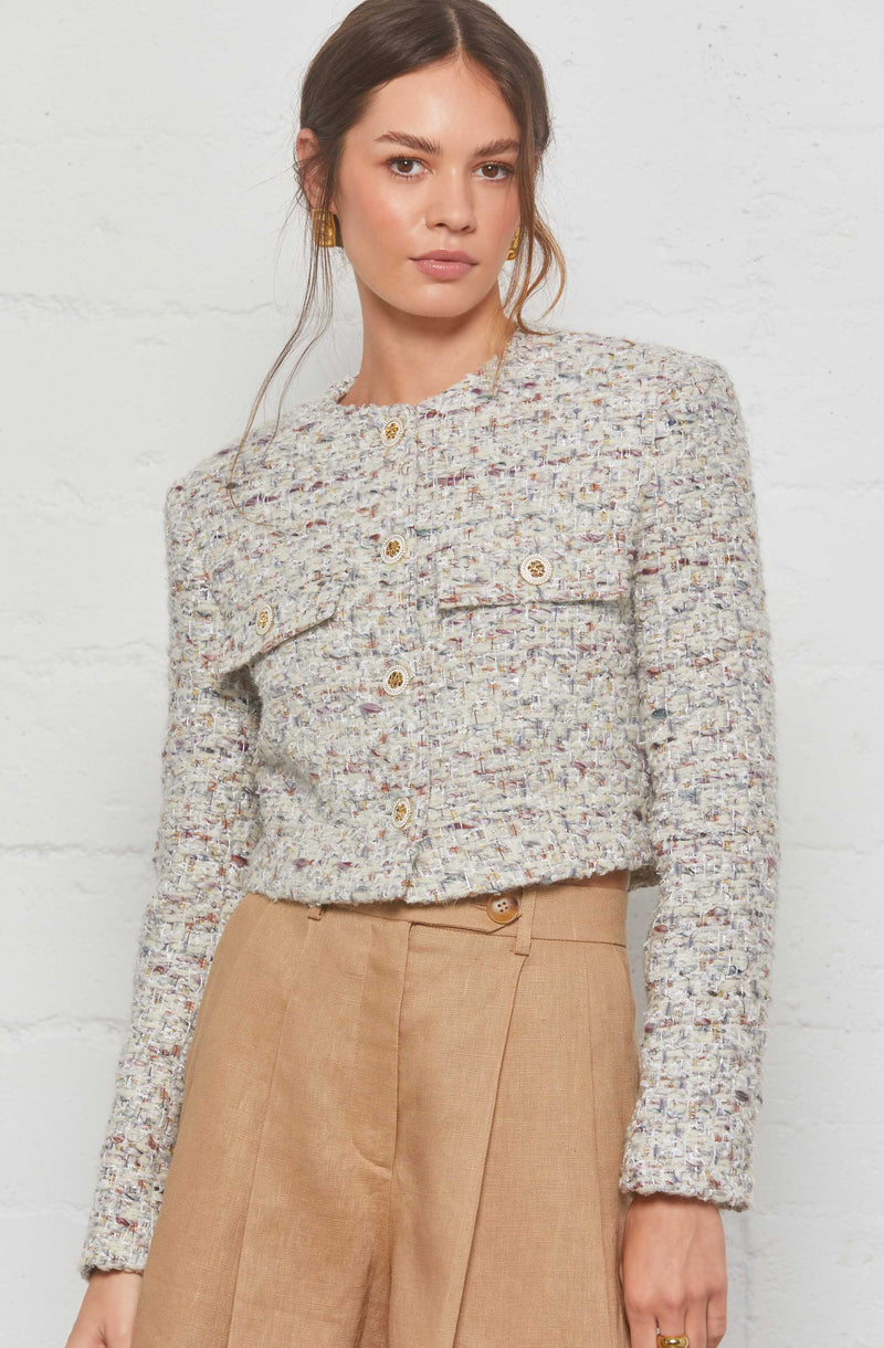 A woman wearing a textured, multicolored tweed cropped jacket with large buttons, paired with high-waisted beige tailored trousers.