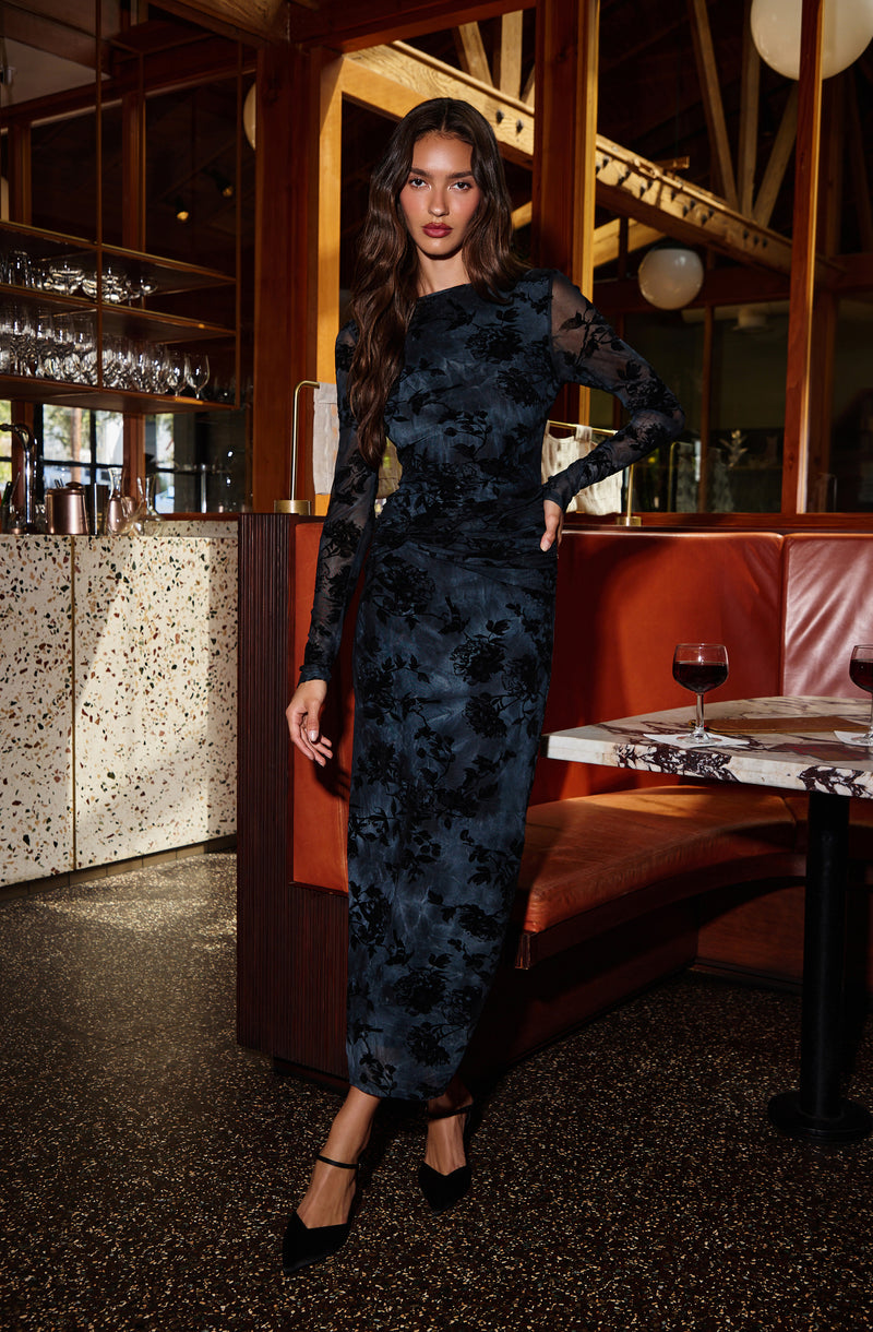 Woman in a navy blue floral lace long dress with sheer sleeves and black high heels.