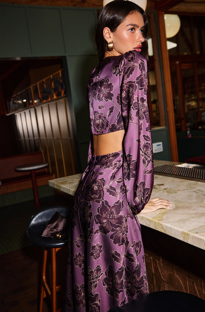 Woman in a purple floral satin dress with puffed long sleeves, showing side and back details.