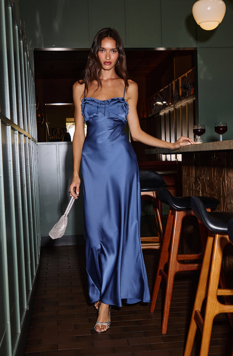 Woman in a shiny blue satin slip dress with ruffle details and spaghetti straps.