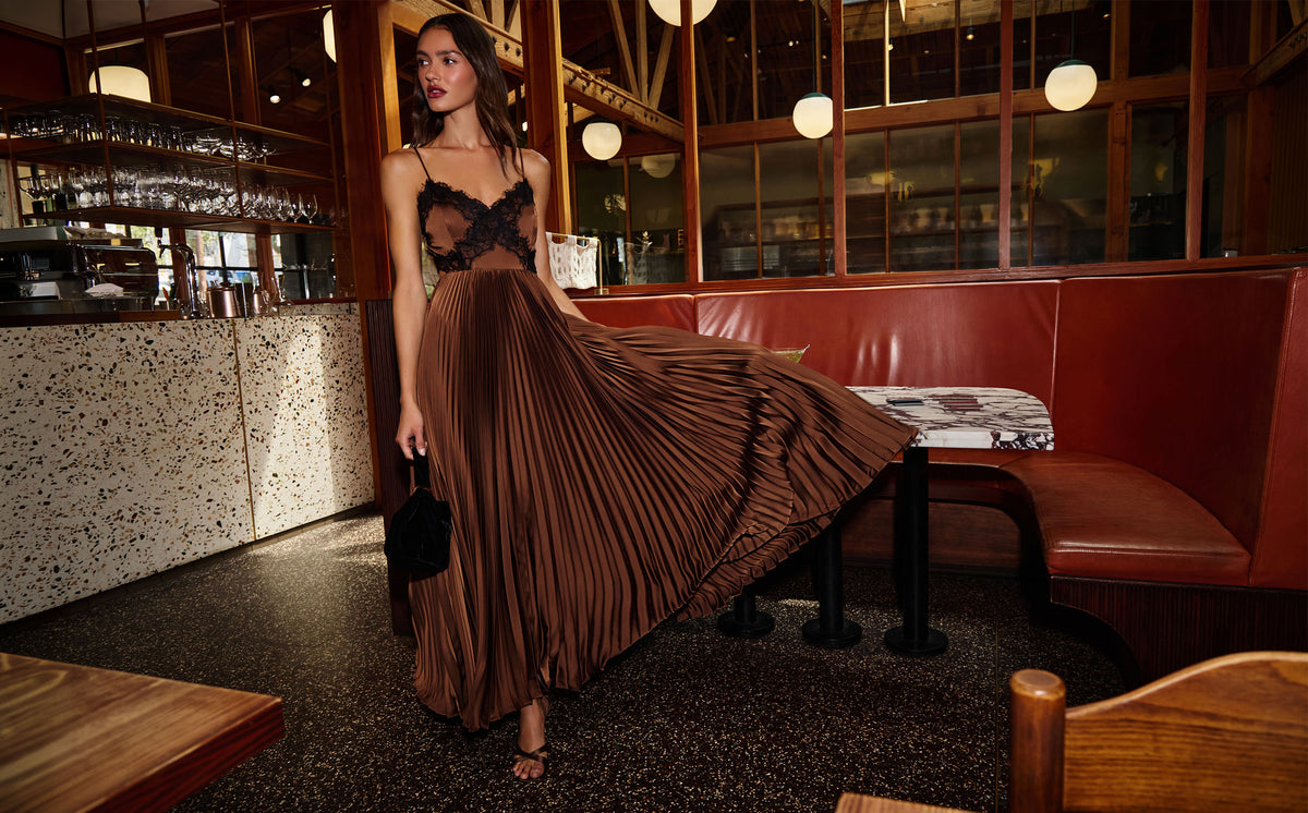 Woman in a black lace top and brown pleated maxi skirt seated in a restaurant.