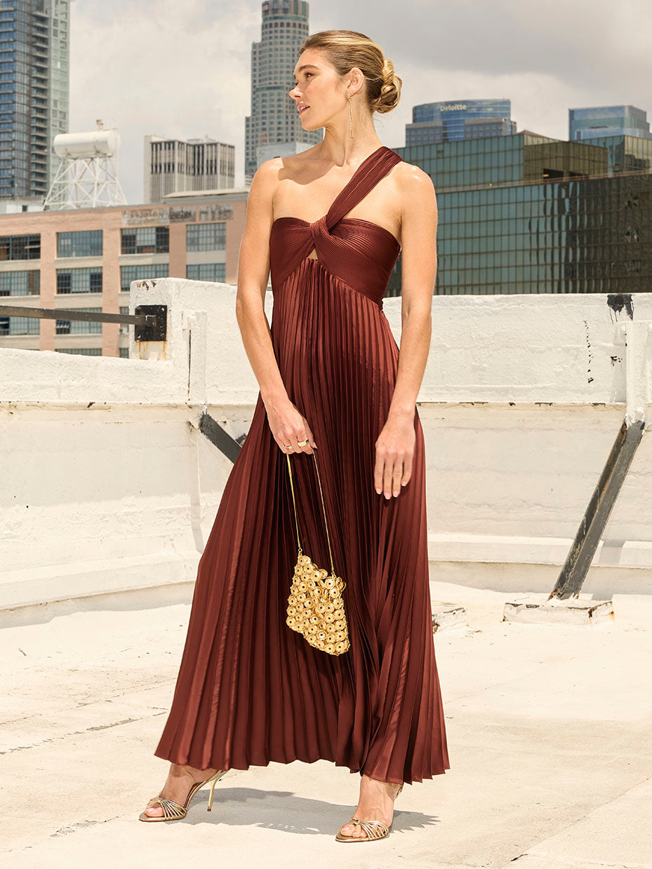 Woman in a one-shoulder, pleated, dark red/burgundy gown with a knotted strap.