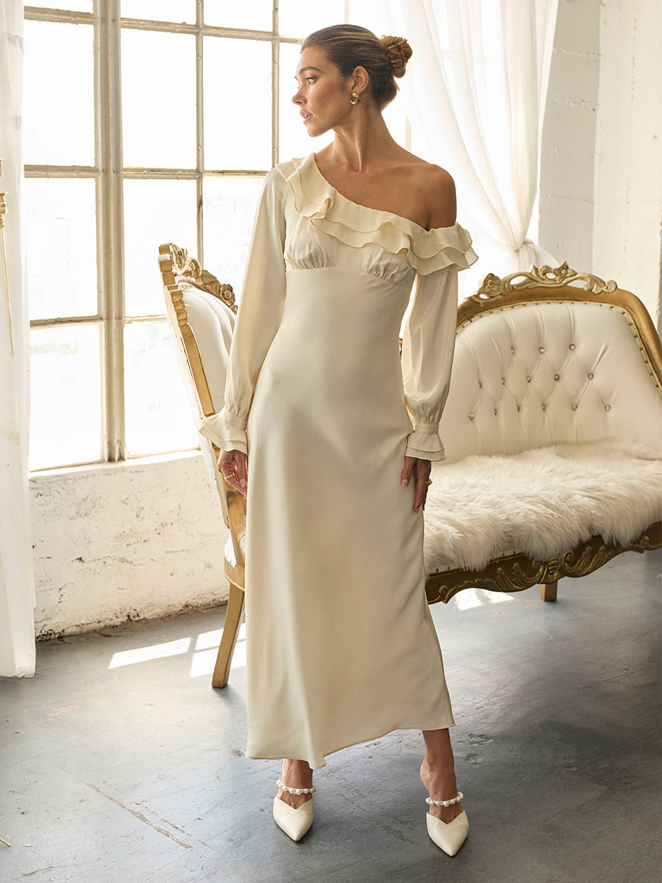 Woman in cream satin gown with ruffled one-shoulder neckline and long puff sleeves, paired with matching heels.