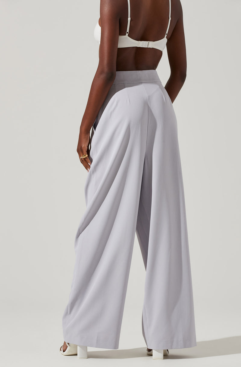 A person wearing high-waisted, wide-leg, light gray trousers paired with a white bra top. The bra top features thin straps and a clasp closure at the back. The outfit combines minimalistic, elegant styles with the focus on the clothing's sleek design and neutral tones.