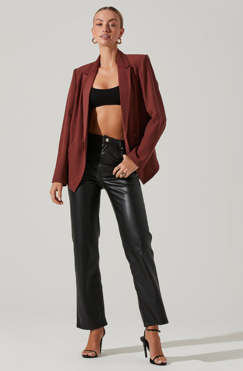 A woman is wearing a black crop top, a burgundy blazer, high-waisted black leather pants, and black high-heeled sandals.